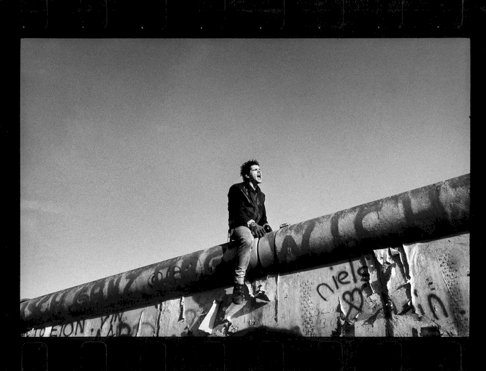 Between the Brandenburg Gate and Potsdamer Platz, a young man sits on the wall between East and West Berlin. West Berlin, Germany, November 11th, 1989 © Raymond Depardon/Magnum Photos
